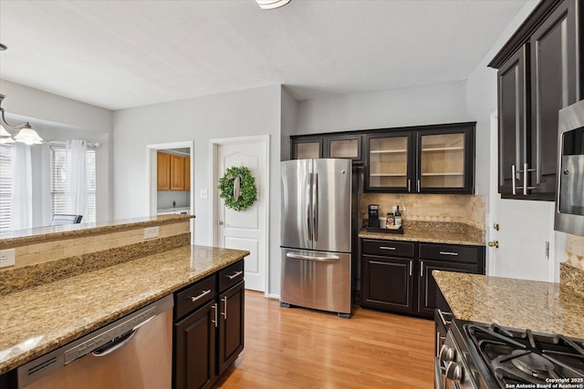 kitchen featuring appliances with stainless steel finishes, backsplash, dark brown cabinetry, light stone counters, and light wood-type flooring