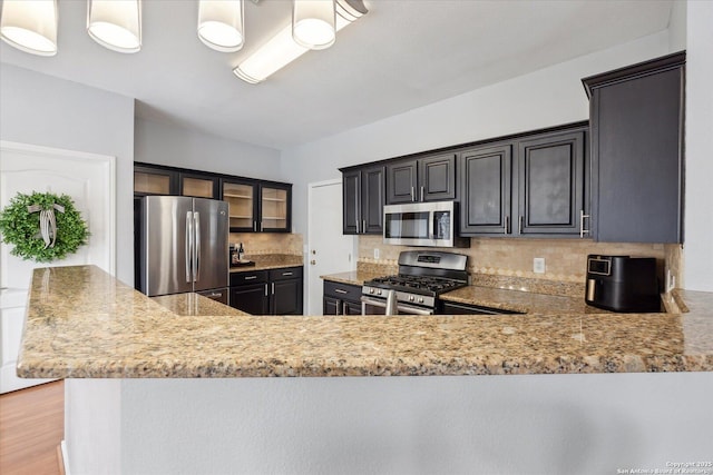 kitchen featuring pendant lighting, decorative backsplash, kitchen peninsula, stainless steel appliances, and light hardwood / wood-style flooring