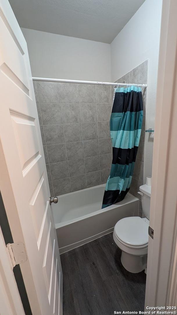 bathroom with hardwood / wood-style floors, shower / bath combo with shower curtain, and toilet