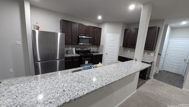 kitchen featuring sink, light stone counters, dark brown cabinets, stainless steel appliances, and decorative backsplash