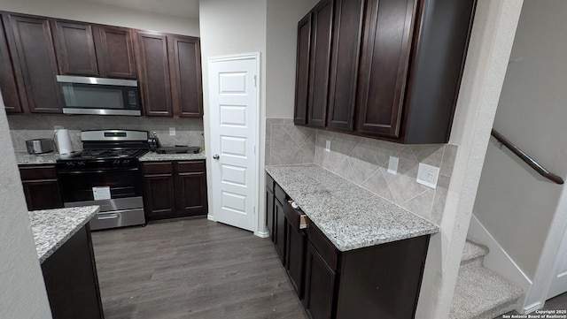 kitchen featuring stainless steel appliances, dark brown cabinets, dark wood-type flooring, and light stone counters