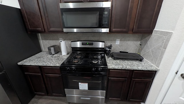 kitchen featuring tasteful backsplash, light stone countertops, stainless steel appliances, and dark brown cabinetry