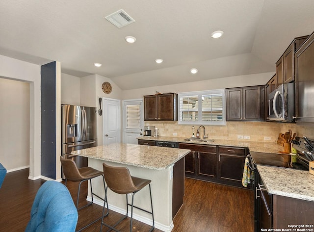 kitchen featuring sink, vaulted ceiling, appliances with stainless steel finishes, a kitchen island, and decorative backsplash