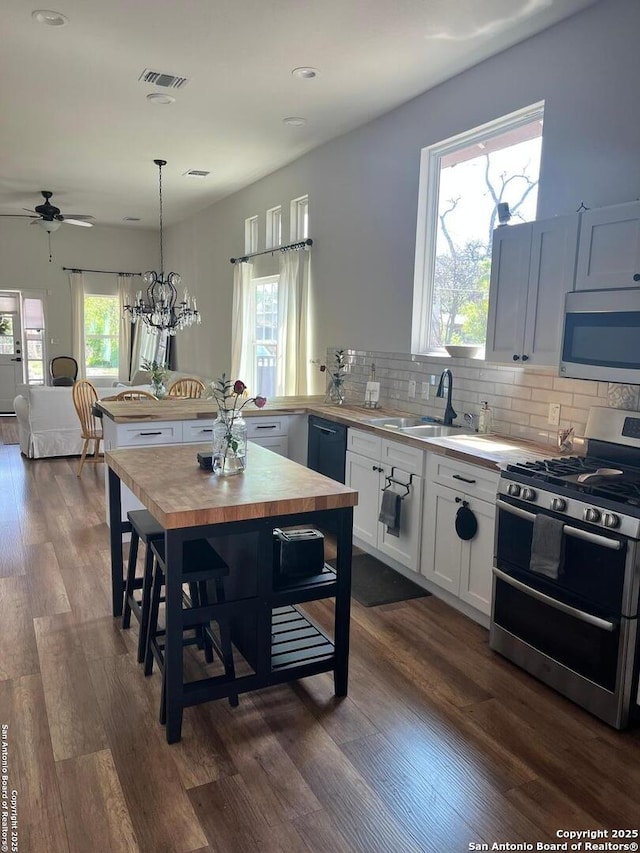 kitchen featuring pendant lighting, wooden counters, appliances with stainless steel finishes, white cabinets, and decorative backsplash