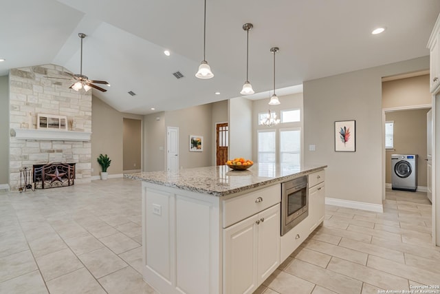 kitchen with a stone fireplace, stainless steel microwave, white cabinetry, washer / dryer, and a center island