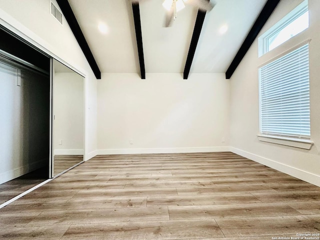 unfurnished bedroom featuring vaulted ceiling with beams, a closet, and light wood-type flooring