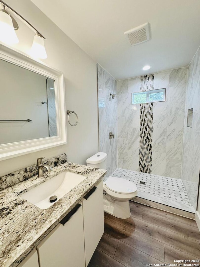 bathroom featuring hardwood / wood-style flooring, vanity, a tile shower, and toilet