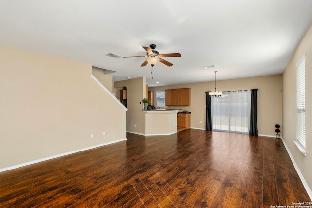 unfurnished living room featuring a healthy amount of sunlight, dark hardwood / wood-style flooring, and ceiling fan with notable chandelier