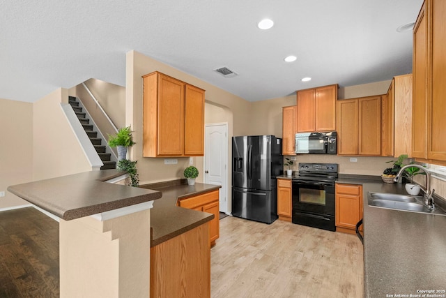 kitchen featuring a kitchen bar, sink, kitchen peninsula, light hardwood / wood-style floors, and black appliances