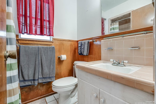 bathroom featuring tile patterned flooring, vanity, wood walls, and toilet