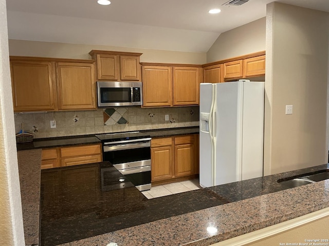 kitchen featuring lofted ceiling, sink, backsplash, stainless steel appliances, and dark stone counters