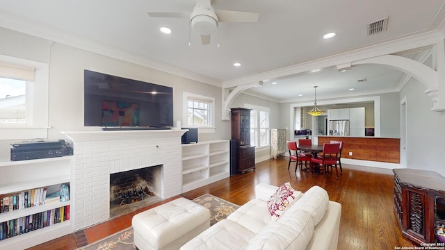 living room with dark wood-type flooring, ceiling fan, ornamental molding, and a fireplace