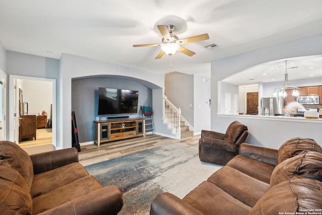 living room with ceiling fan with notable chandelier and light hardwood / wood-style flooring