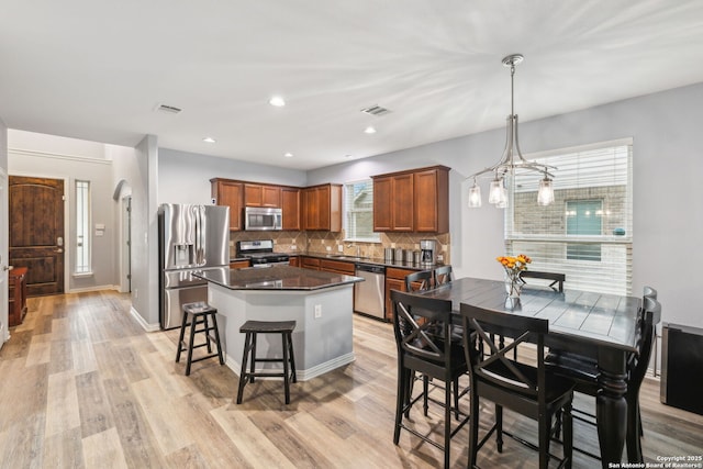 kitchen with hanging light fixtures, decorative backsplash, light wood-type flooring, and appliances with stainless steel finishes