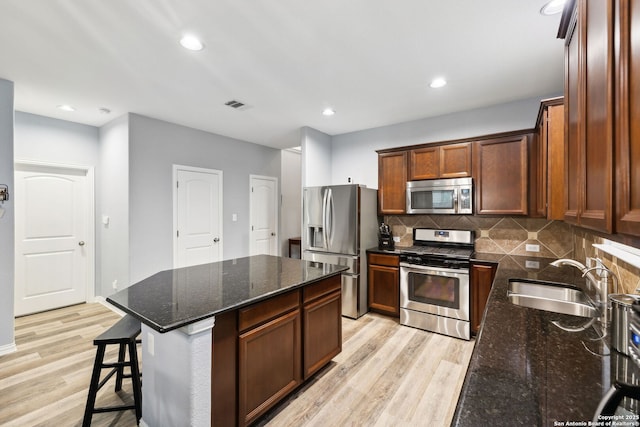 kitchen with a kitchen island, sink, dark stone countertops, light hardwood / wood-style floors, and stainless steel appliances