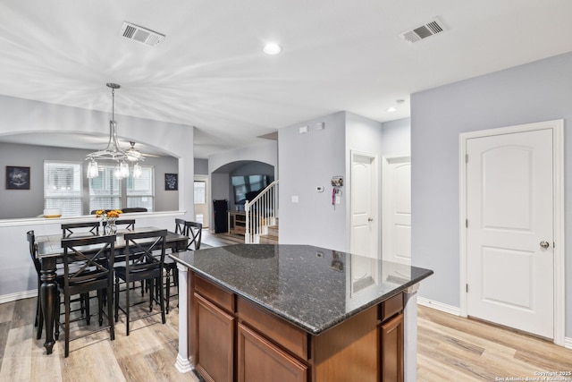 kitchen featuring light hardwood / wood-style flooring, a center island, decorative light fixtures, dark stone counters, and a chandelier