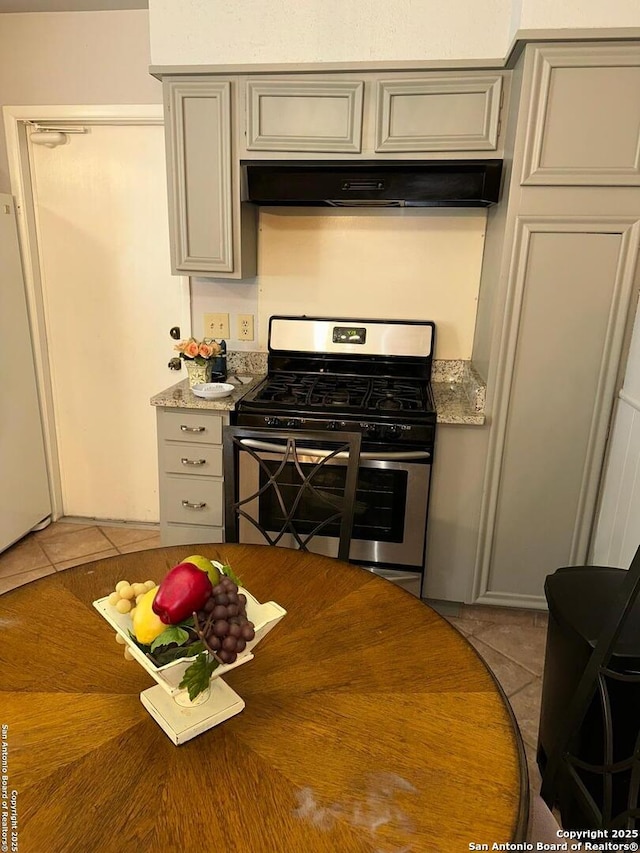 kitchen featuring light tile patterned flooring, white fridge, exhaust hood, gas range, and light stone countertops