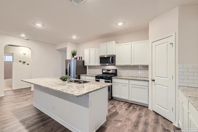 kitchen featuring appliances with stainless steel finishes, hardwood / wood-style floors, white cabinets, a kitchen island with sink, and light stone countertops