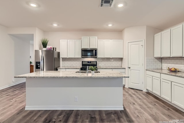 kitchen featuring light stone counters, stainless steel appliances, an island with sink, and white cabinets