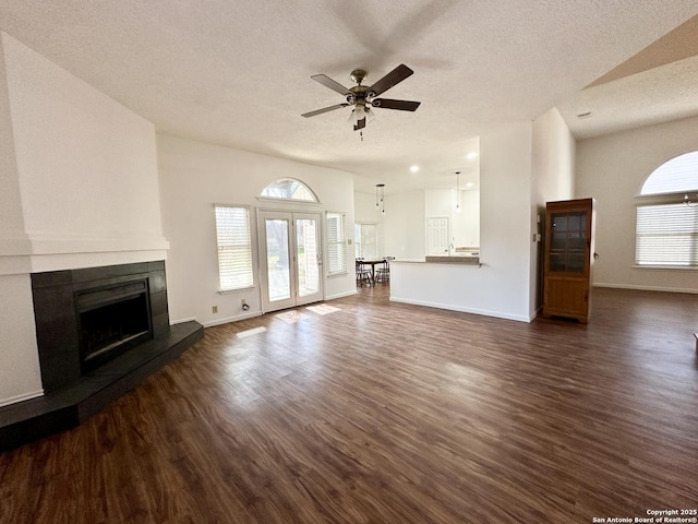 unfurnished living room featuring a tiled fireplace, ceiling fan, dark wood-type flooring, and a textured ceiling