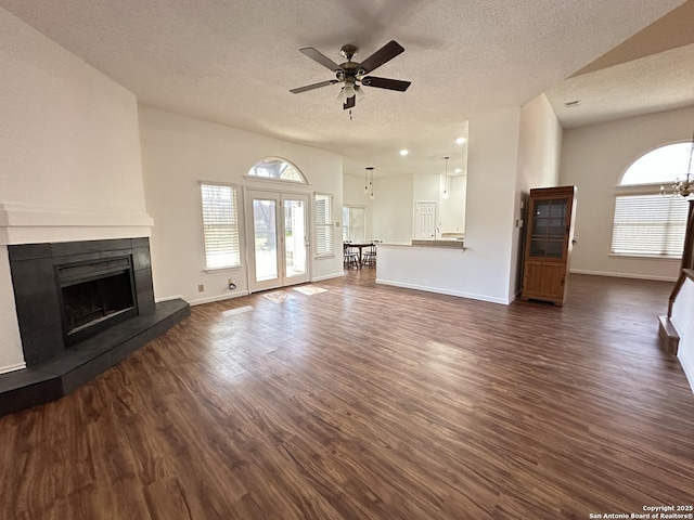 unfurnished living room featuring dark hardwood / wood-style floors, a tiled fireplace, ceiling fan with notable chandelier, and a textured ceiling