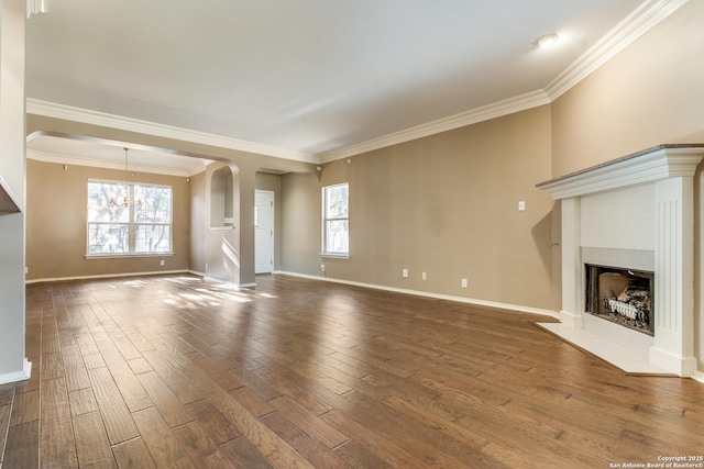 unfurnished living room with a tiled fireplace, crown molding, dark wood-type flooring, and plenty of natural light