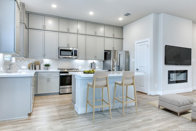 kitchen featuring gray cabinets, an island with sink, and appliances with stainless steel finishes