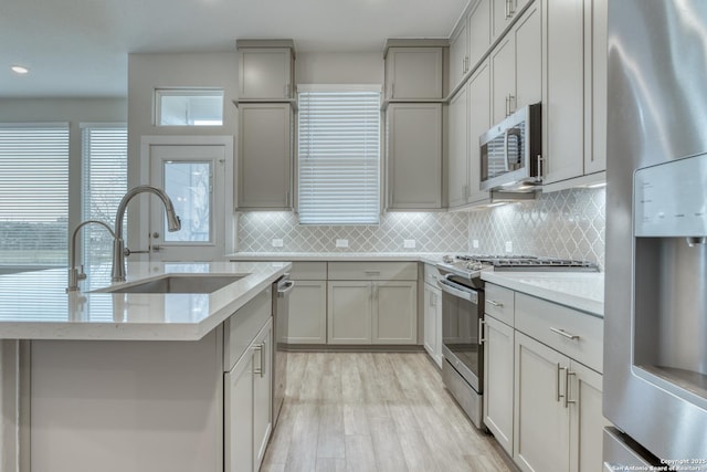 kitchen featuring appliances with stainless steel finishes, gray cabinetry, light hardwood / wood-style floors, backsplash, and sink