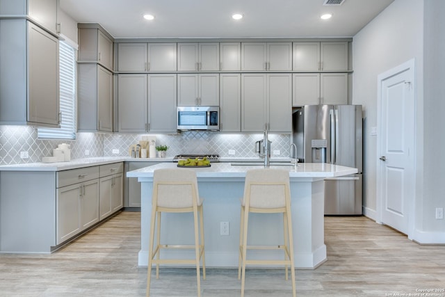 kitchen with sink, gray cabinetry, light hardwood / wood-style floors, a breakfast bar area, and a kitchen island with sink