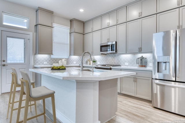 kitchen with an island with sink, appliances with stainless steel finishes, sink, and gray cabinetry