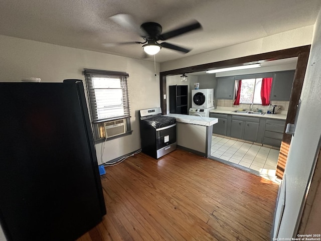 kitchen with stacked washer and dryer, sink, black refrigerator, gray cabinetry, and stainless steel range with gas cooktop