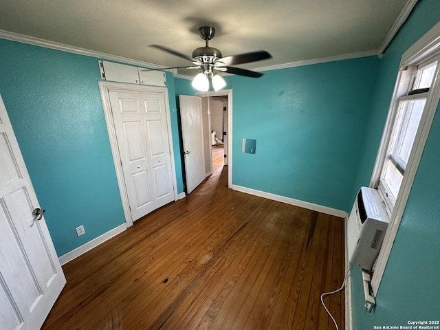 unfurnished bedroom featuring crown molding, dark wood-type flooring, ceiling fan, a wall unit AC, and a closet