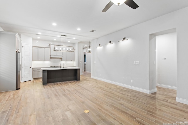 kitchen with an island with sink, light wood-type flooring, stainless steel refrigerator, and decorative light fixtures