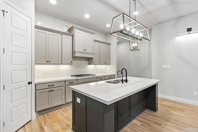 kitchen with sink, tasteful backsplash, light hardwood / wood-style flooring, gray cabinets, and pendant lighting