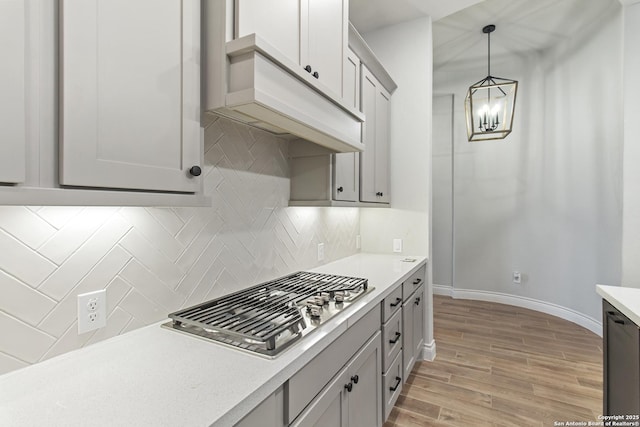 kitchen featuring stainless steel gas cooktop, tasteful backsplash, a chandelier, pendant lighting, and light hardwood / wood-style floors