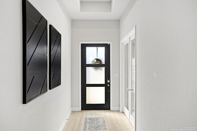 doorway to outside with a raised ceiling and light hardwood / wood-style flooring