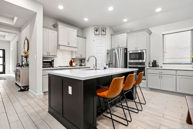 kitchen featuring sink, backsplash, stainless steel appliances, a kitchen breakfast bar, and a center island with sink