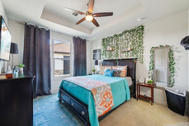 carpeted bedroom with a raised ceiling and ceiling fan