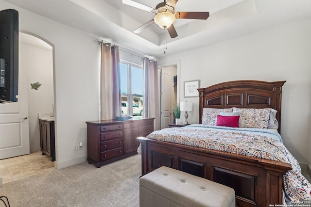 carpeted bedroom with a raised ceiling, ensuite bathroom, and ceiling fan