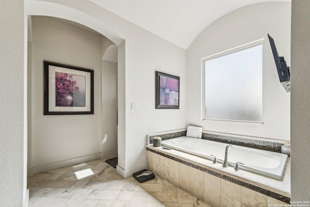 bathroom featuring vaulted ceiling and tiled bath