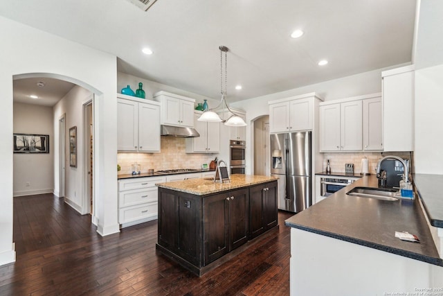 kitchen featuring dark wood-type flooring, sink, decorative light fixtures, an island with sink, and stainless steel appliances