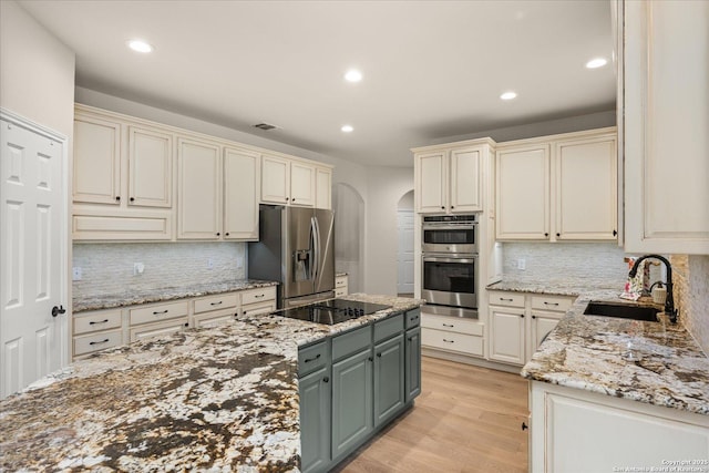 kitchen with arched walkways, cream cabinets, stainless steel appliances, a sink, and light wood-style floors