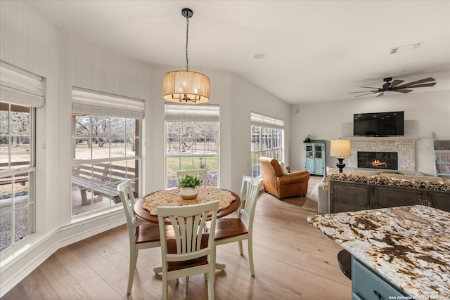 dining space featuring ceiling fan, light wood-style flooring, a fireplace, visible vents, and baseboards