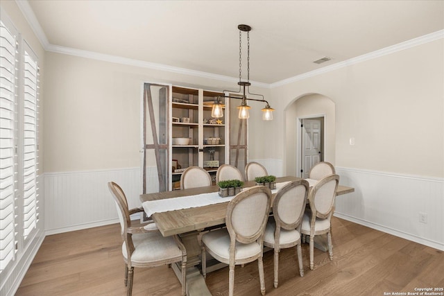 dining space featuring arched walkways, visible vents, light wood-style floors, wainscoting, and crown molding