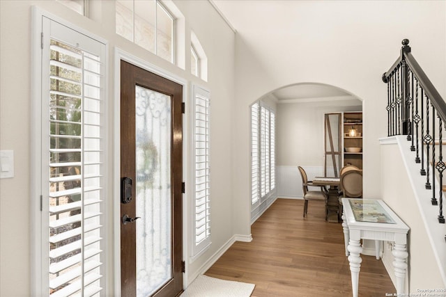 entryway with arched walkways, crown molding, wood finished floors, baseboards, and stairs