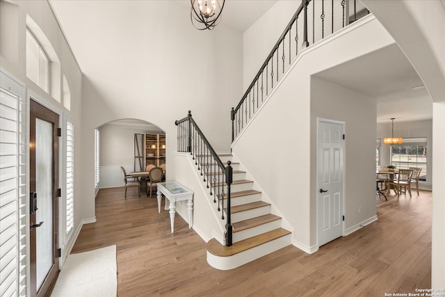 foyer with stairs, arched walkways, a notable chandelier, and wood finished floors