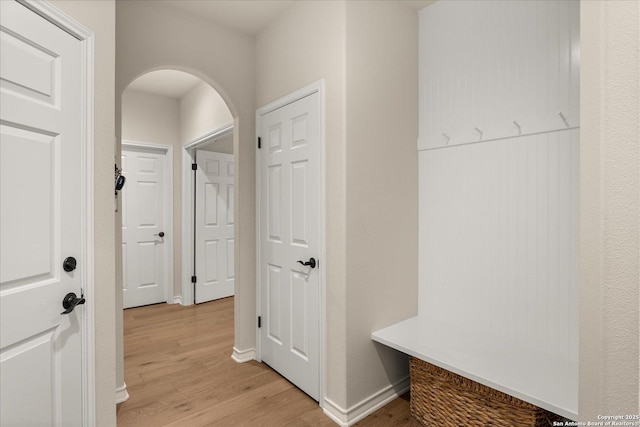 mudroom featuring arched walkways, light wood-style flooring, and baseboards