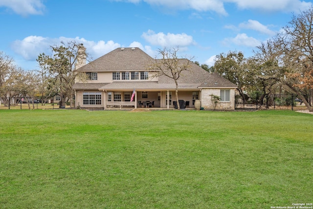 rear view of property featuring a lawn, a patio, stone siding, a chimney, and fence