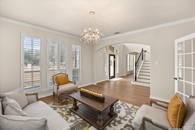 living room featuring arched walkways, visible vents, ornamental molding, wood finished floors, and stairs