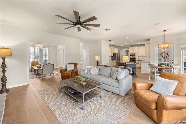 living area with recessed lighting, visible vents, light wood-style floors, baseboards, and ceiling fan with notable chandelier